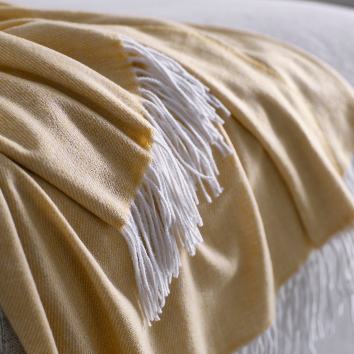 A close-up of a HOLMVI throw in beige-yellow draped over a white bedspread on a bed in a bright room.