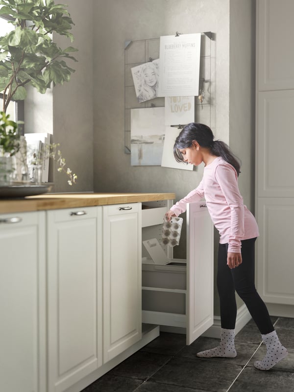 A girl putting garbage in a waste station with HÅLLBAR bin with lid, BODBYN doors in off-white and a FÖRBÄTTRA plinth.