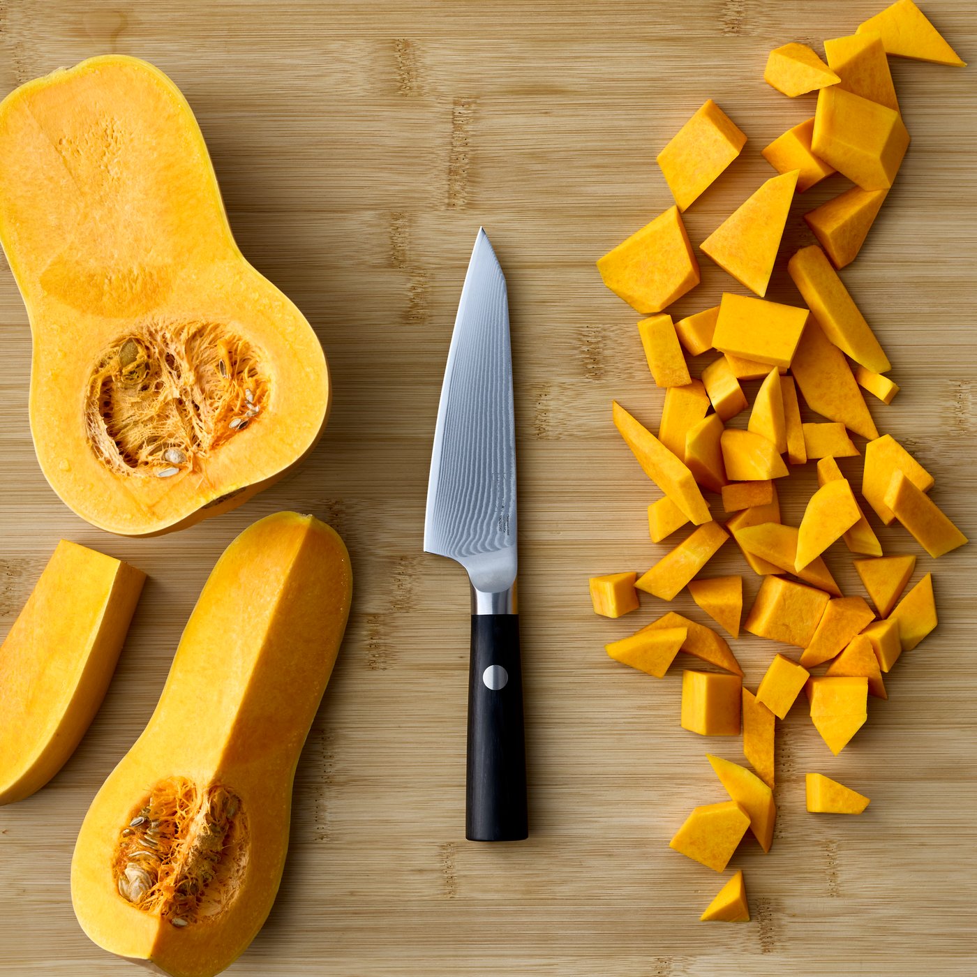 A wooden kitchen counter shows a black FJÄLLRÖDING utility knife made of Damascus steel beside chopped butternut squash.