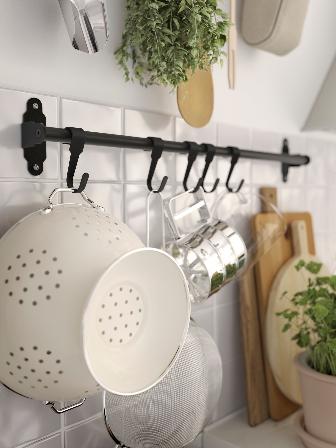 In einer Küche ist eine Wand mit einer Stange mit Haken zu sehen, an denen unterschiedliche Küchenutensilien hängen, wie z. B. ein GEMAK Durchschlag.