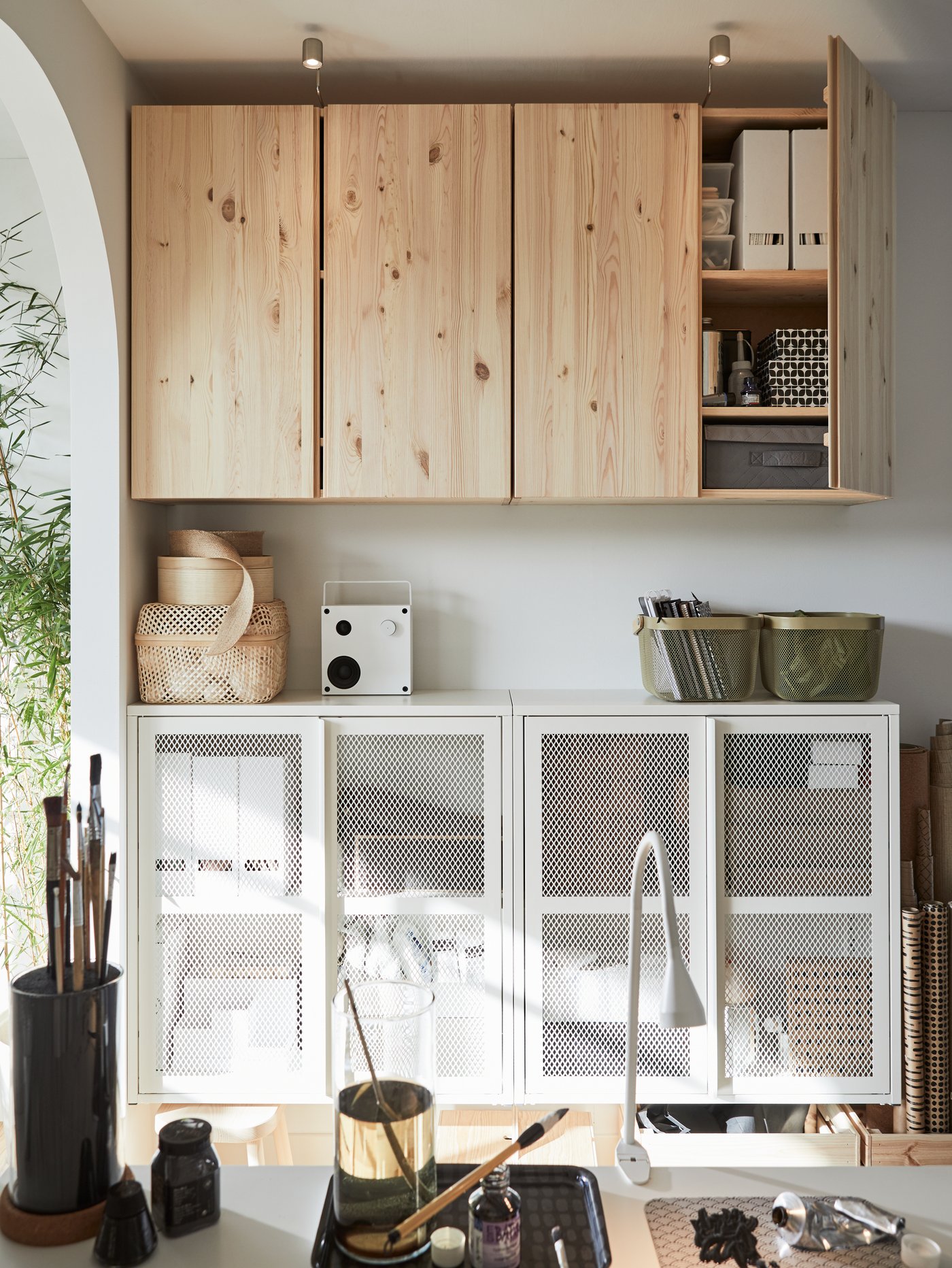 Two wooden storage cabinets hanging on the wall, and two white storage cabinets below it. A speaker and baskets are on it.