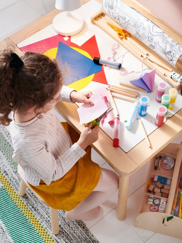 Una niña coloreando y cortando papeles de color en una mesa infantil FLISAT