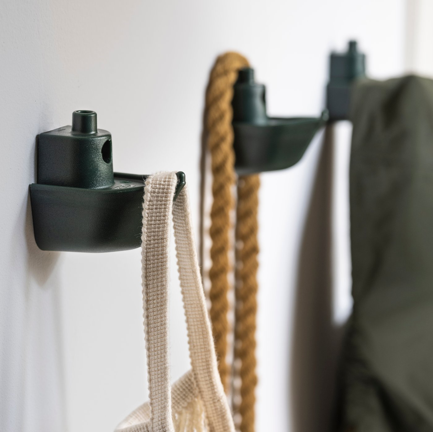 Es sind drei grüne, an der Wand befestigte KNOPARE Haken zu sehen. An zwei hängt eine Tasche und am dritten eine Jacke.