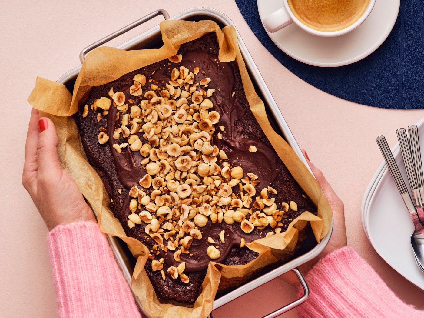 Manos sosteniendo una sartén de brownies con coberturas.