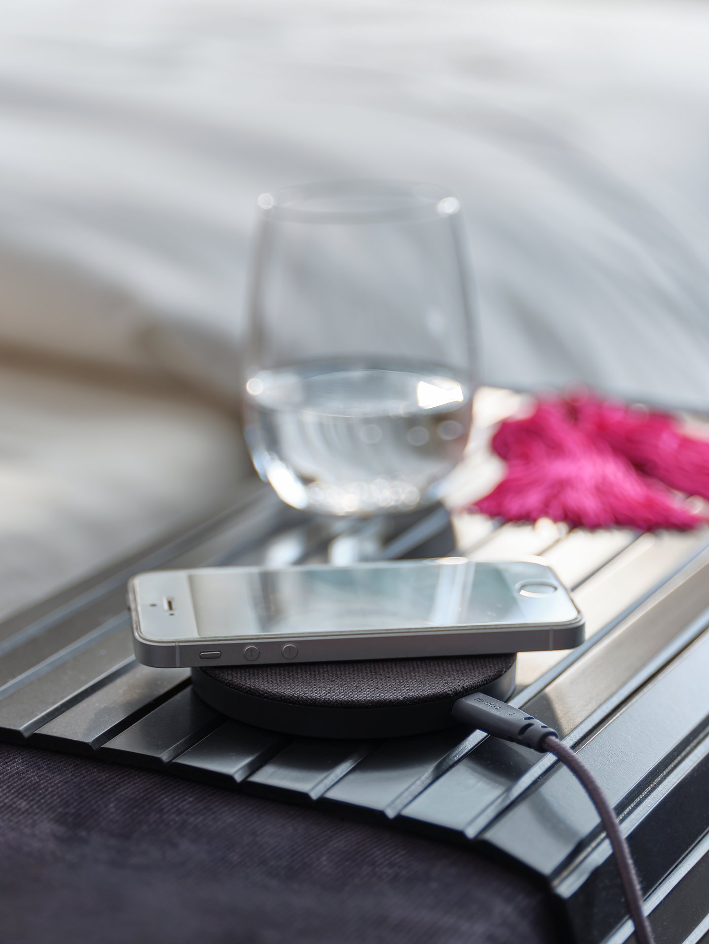 An armrest tray with a glass of water, a textile/grey wireless charger and a smartphone.