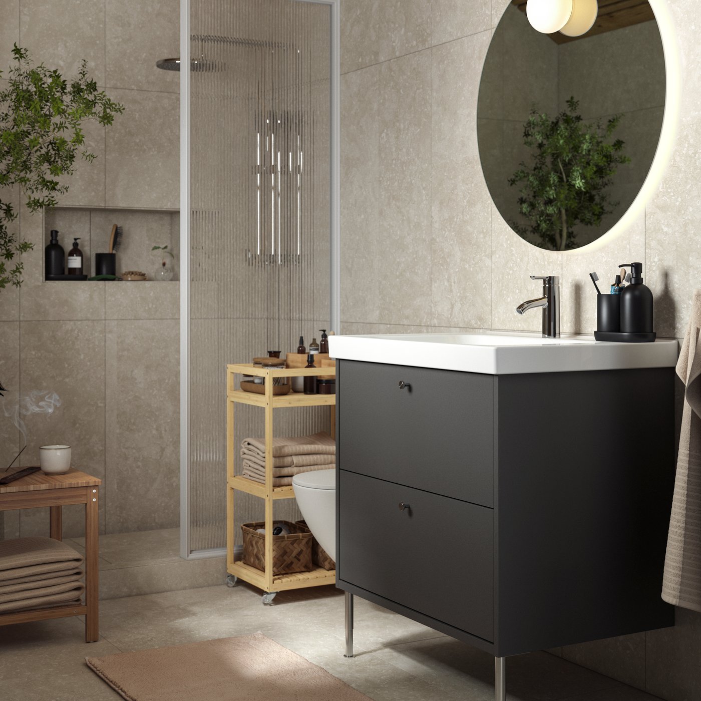 A sunlit zen bathroom with a dark-grey HAVBÄCK drawer and furniture in bamboo. A large green plant in the corner.