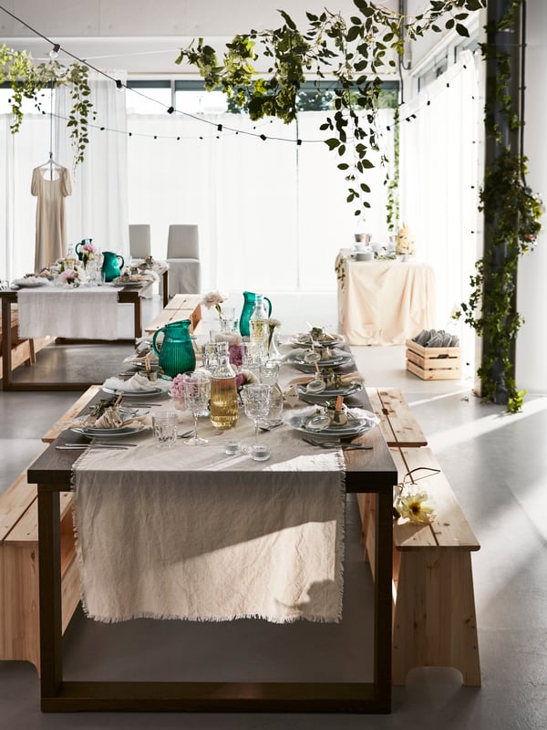 Table festive dressée pour une grande occasion dans un espace ouvert doté de grandes fenêtres et orné de guirlandes lumineuses et de végétaux.