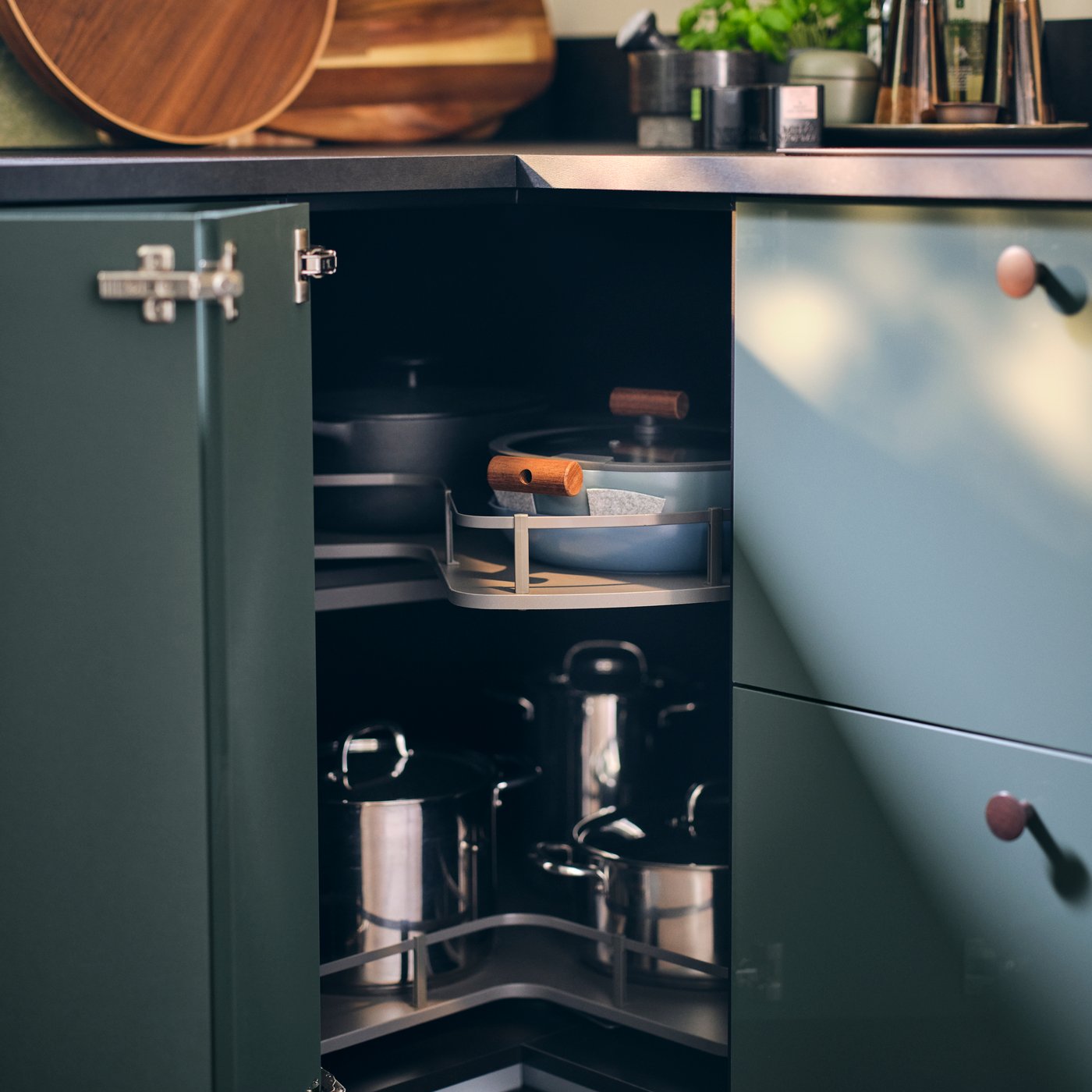 A fold-out door is open to display an UTRUSTA corner base carousel holding diverse pots and pans, and BEDÖMA pan protectors.