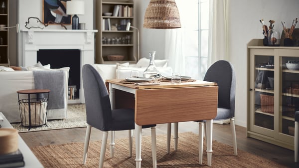 Comedor de la serie HAUGA. Todo en un living con colores tierra y una silla con cubre sillas de color gris oscuro y una vitrina beige donde se guardan libros y decoración.