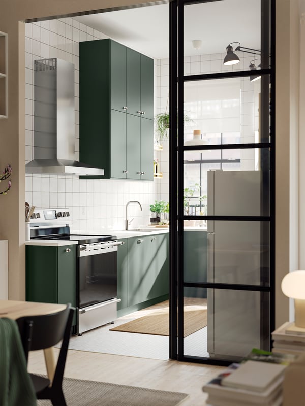 A wide doorway into a kitchen with deep green HAVSTORP kitchen fronts and a white marble effect/laminate EKBACKEN countertop.