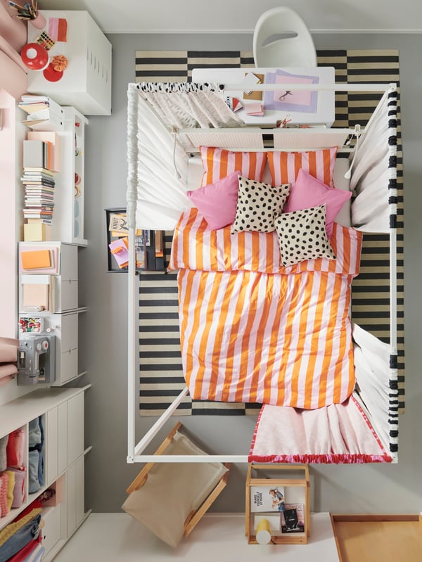 An overhead view of a bedroom with a VITARNA four-poster bed in the middle covered in pink/orange SLÅNHÖSTMAL bed linen.