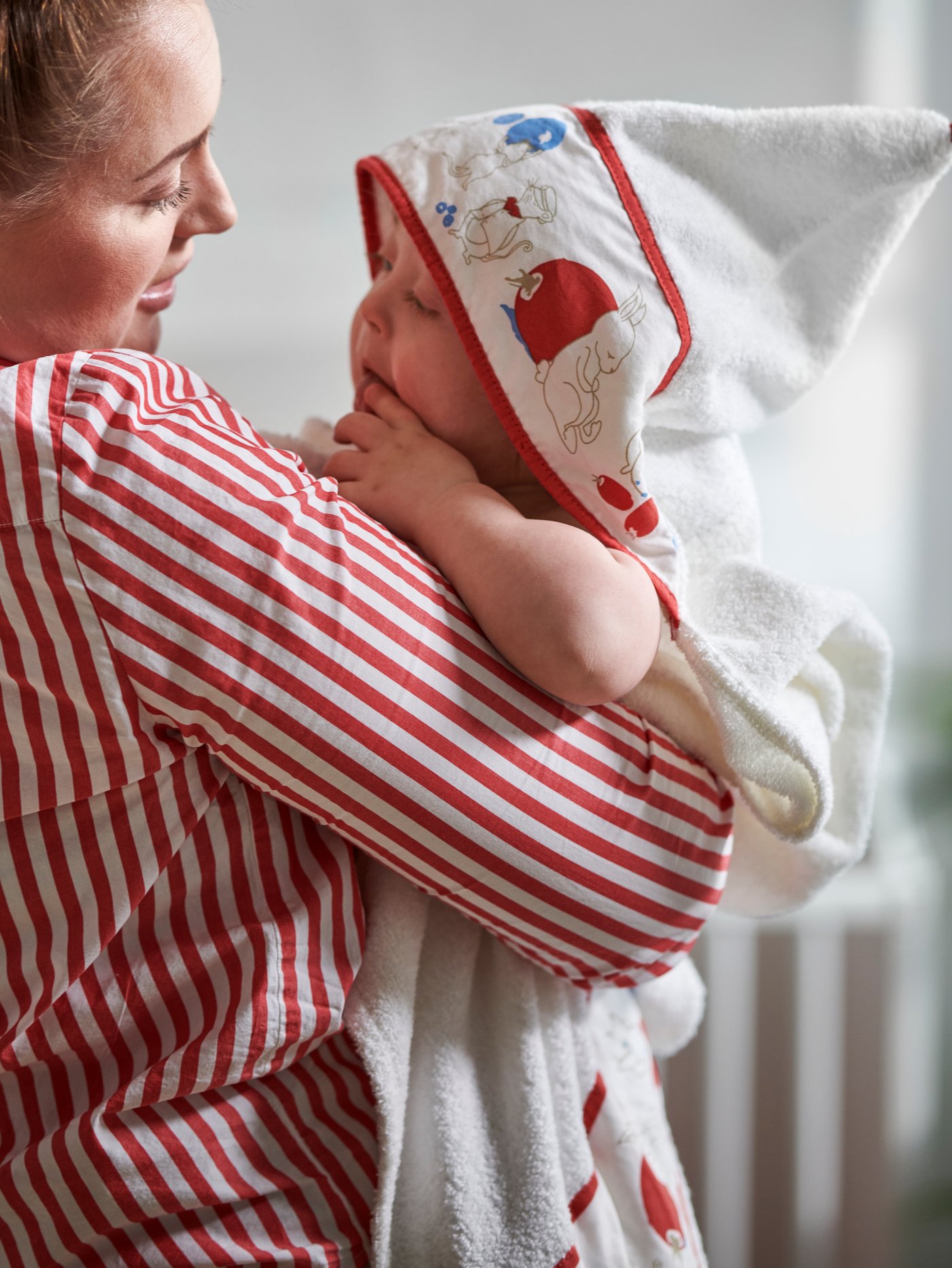 Maman en chemisier rayé embrassant son bébé enveloppé dans une serviette à capuche IKEA.
