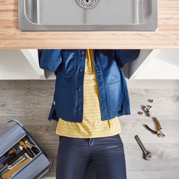 An IKEA co-worker installs a kitchen sink from underneath the worktop, with tools close at hand.