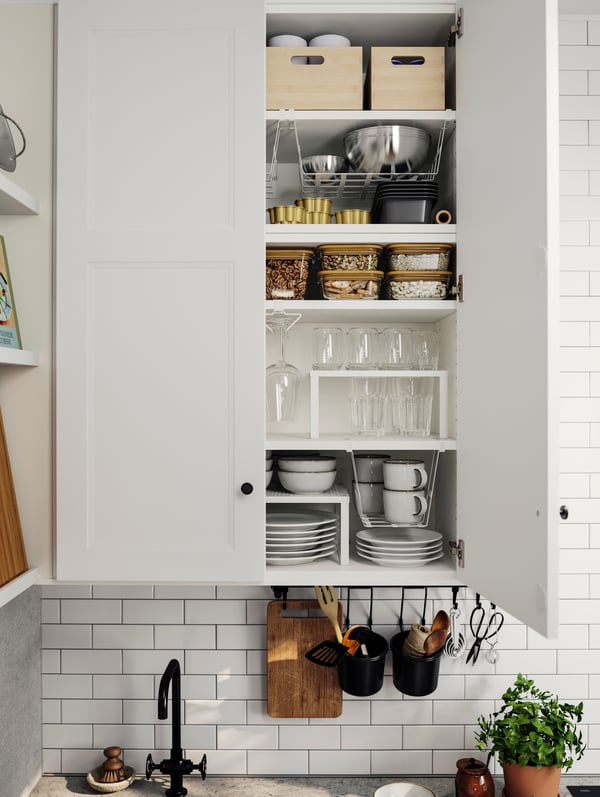 AXSTAD matte white kitchen fronts with an open cabinet showing neatly organised glasses, bowls, and pantry items in jars.