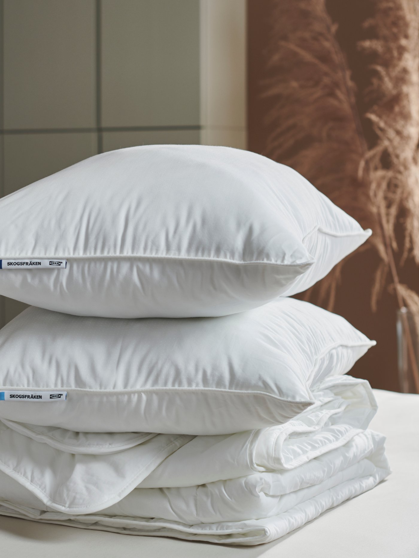 Dua bantal SKOGSFRÄKEN berbeza ditindan di atas satu sama lain pada duvet STJÄRNBRÄCKA yang dilipat di atas katil.