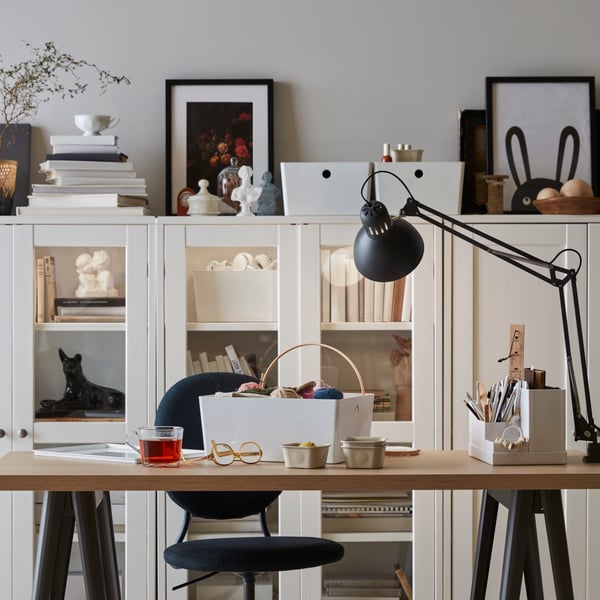 A white-and-birch LAGKAPTEN desk with dried plants on paper on its tilted tabletop. A white lamp is clamped to the table.