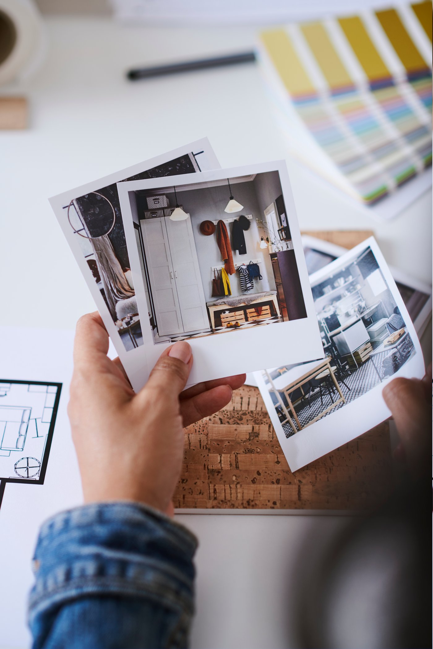 Une main tient un certain nombre de polaroïds inspirants avec des images de différents intérieurs. En arrière-plan se trouvent du matériel de dessin et un éventail de couleurs.