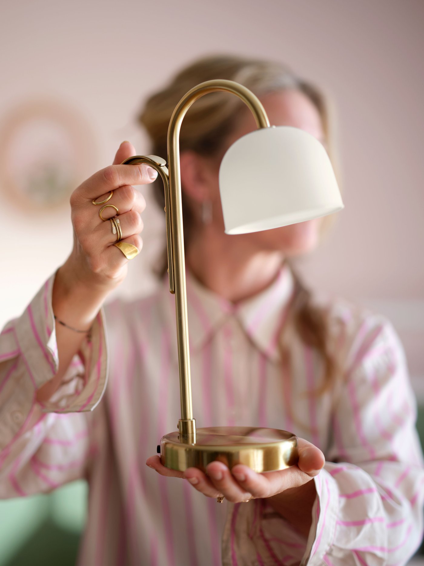 A person holds a classic, portable table lamp, featuring a golden brass finish and an elegant, white bell-shaped shade.