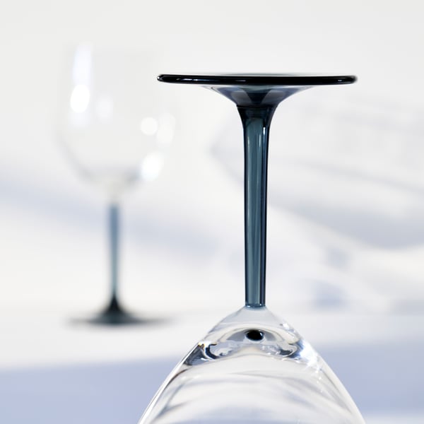 A closeup of the grey stem of a RÖDRÄKA wine glass, which is standing upside down on a bright surface.