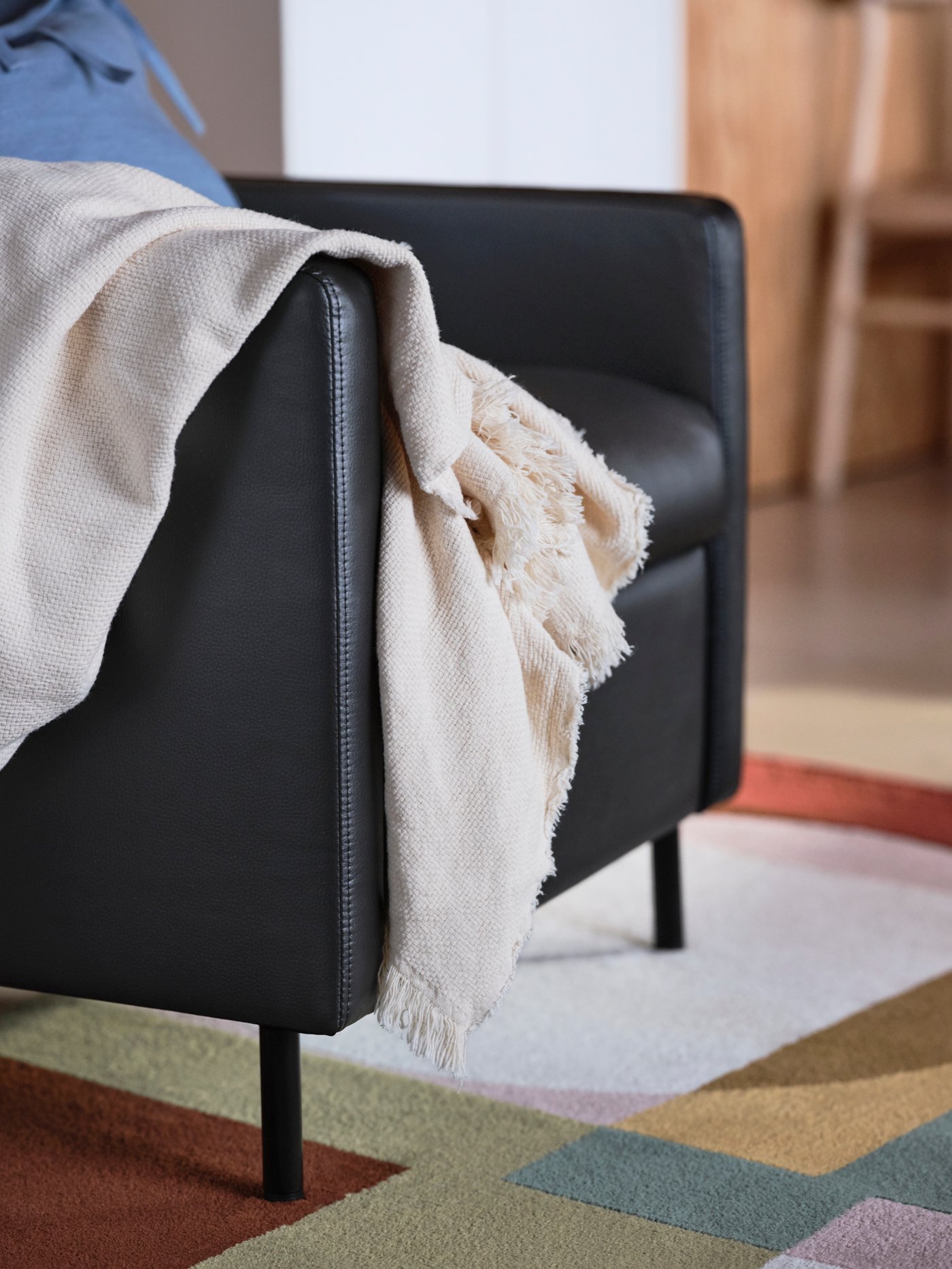 A multicoloured rug with a geometrical pattern, a black GISTAD recliner, a blue cushion, and a white ODDRUN throw.