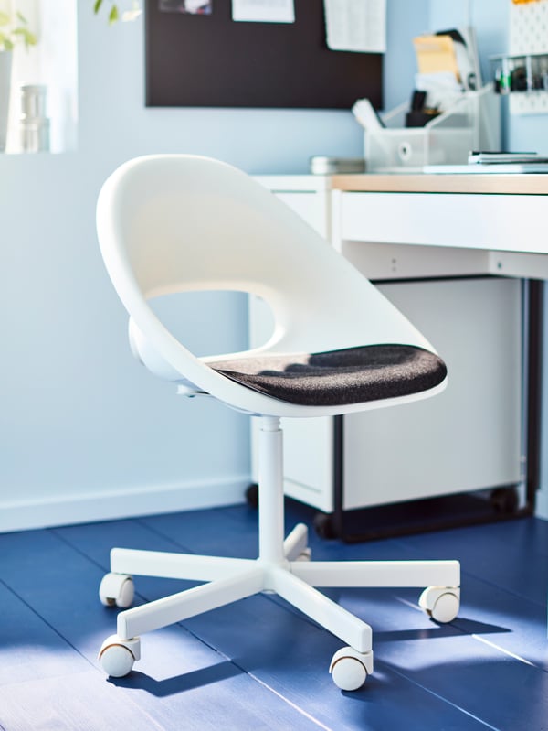 A white swivel chair with dark grey seat pad stands on a blue floor next to a white desk.