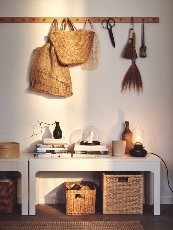 Handcrafted items hanging from a row of HÖVOLM six-knob racks on a white wall. Below are benches with decorative storage.