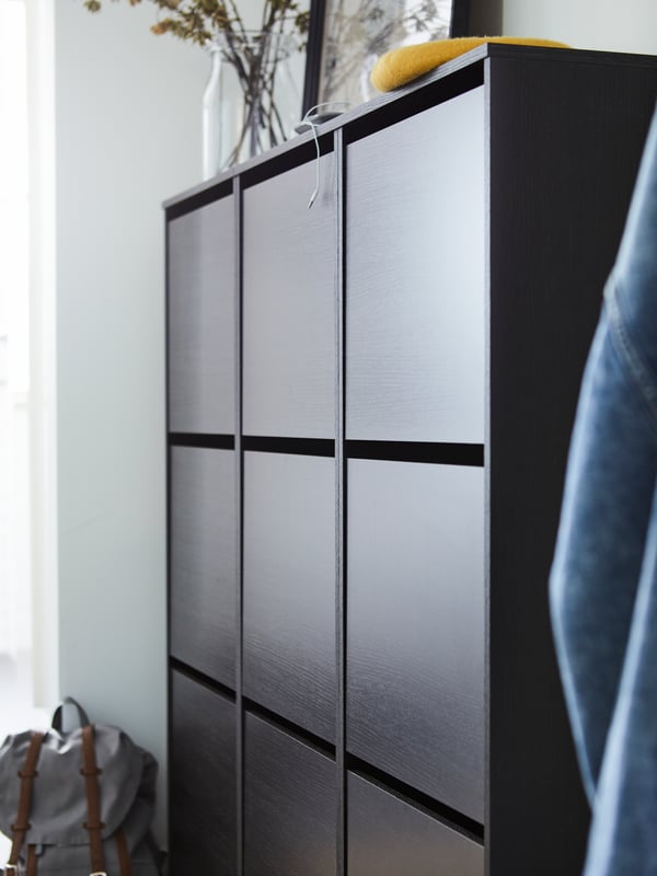 Three black/brown BISSA shoe cabinets with three compartments, a frame and a glass vase on top of them, and a backpack.
