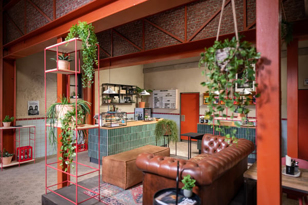  Een industriële zithoek met een bank, metalen rekken en ENHET opbergmeubels, aangevuld met hangplanten, creëert een warme loftsfeer met oranje accenten