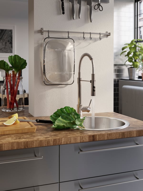 A wooden worktop with an inset sink and a mixer tap that’s turned on to wash rhubarb placed in the sink.