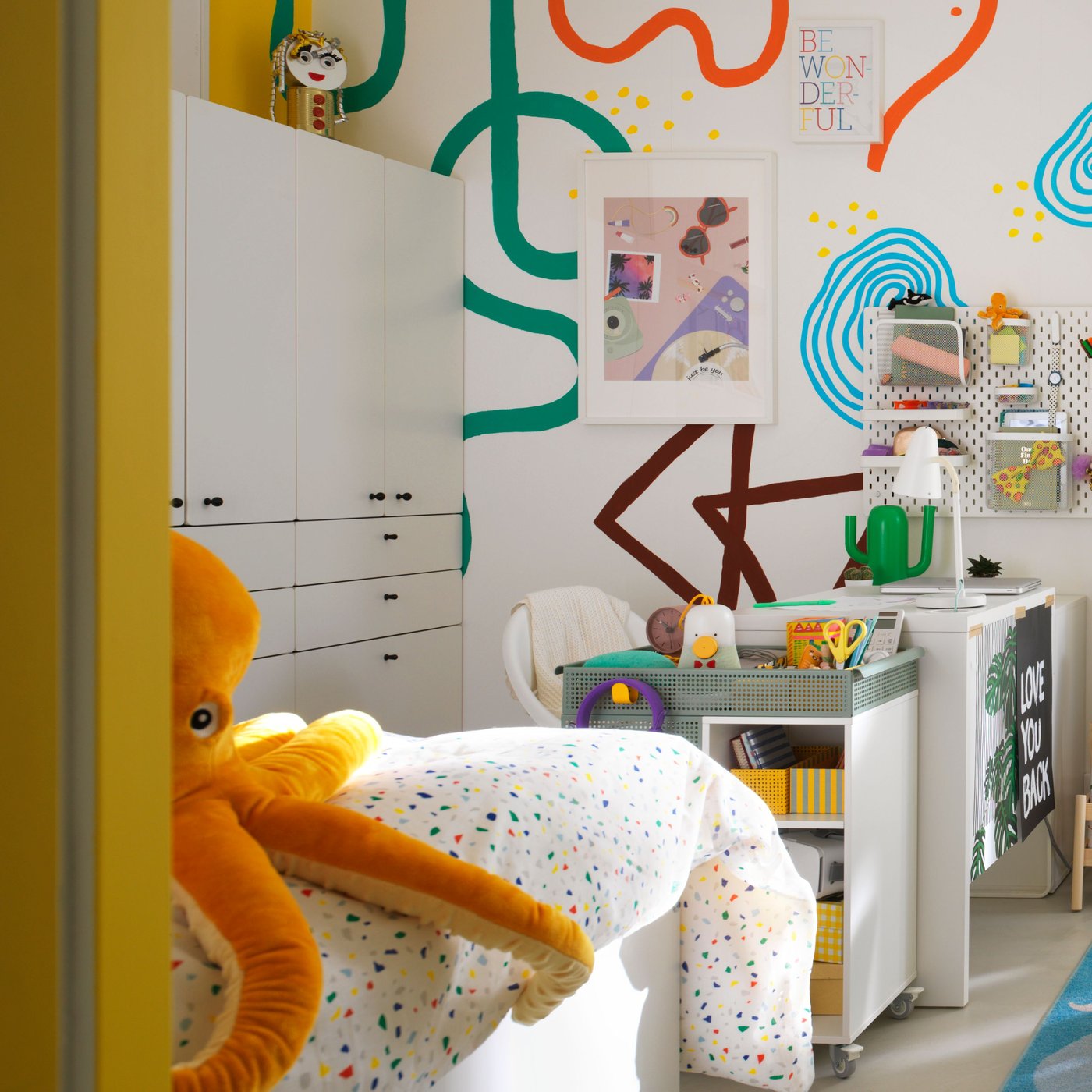 A childrens bedroom with a bed, desk, large soft octopus toy and art supplies.