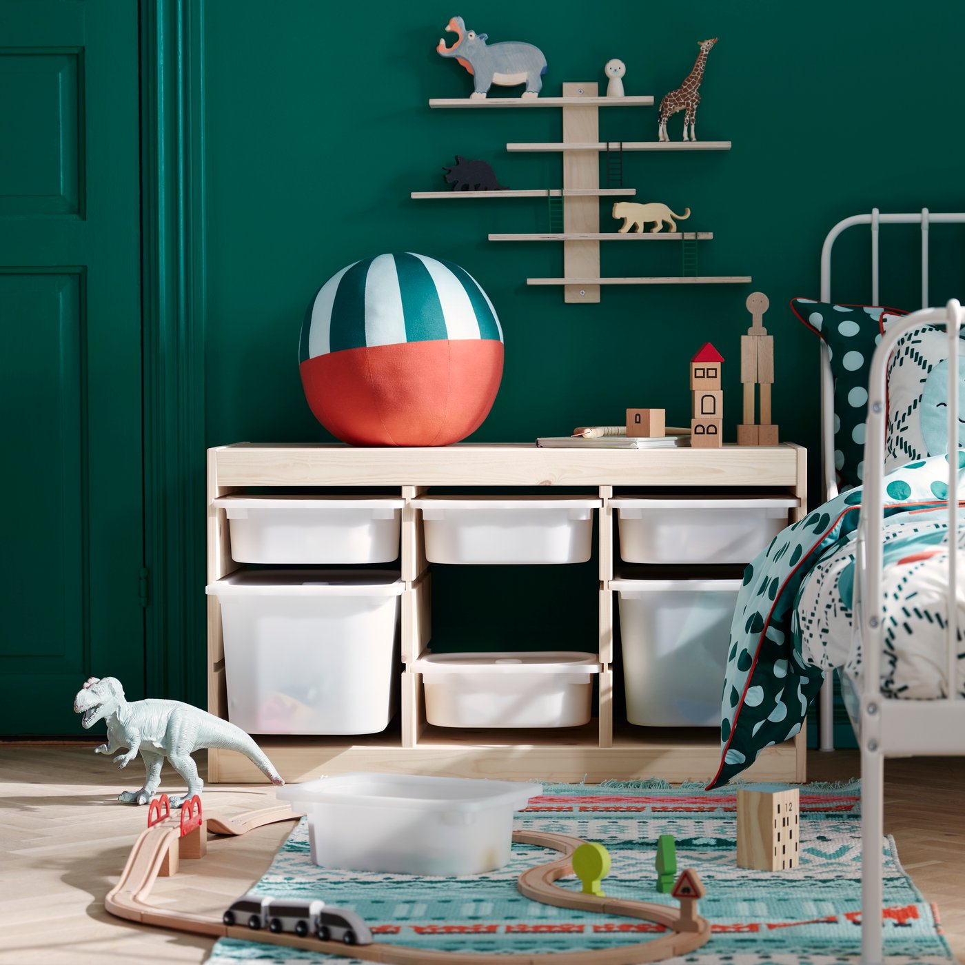 Un dormitorio infantil con un mueble para juguetes TROFAST con cajones plásticos y sobre él una repisa de madera.