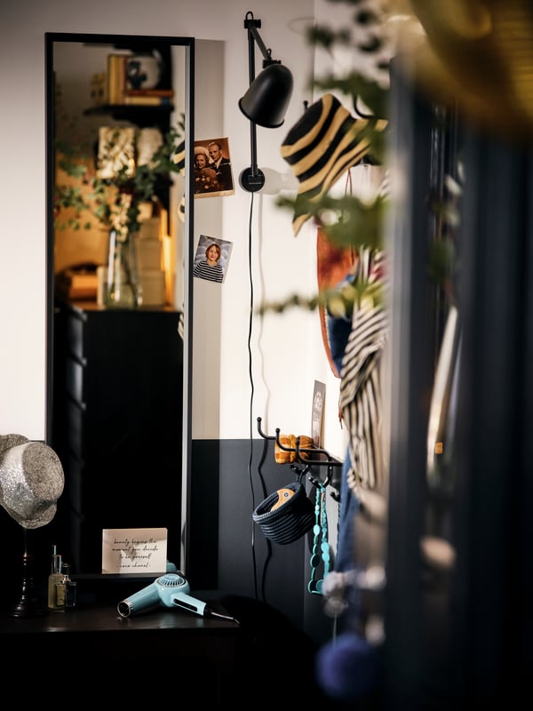 Un coin de chambre avec un miroir NISSEDAL noir et une lampe SKURUP noire murale au milieu de plusieurs éléments décoratifs.