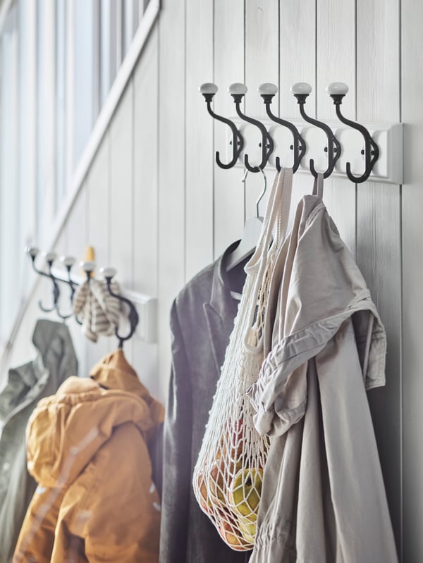 Two white LANDKRABBA racks with 5 hooks with clothes hanging from them are mounted on the side of a staircase.