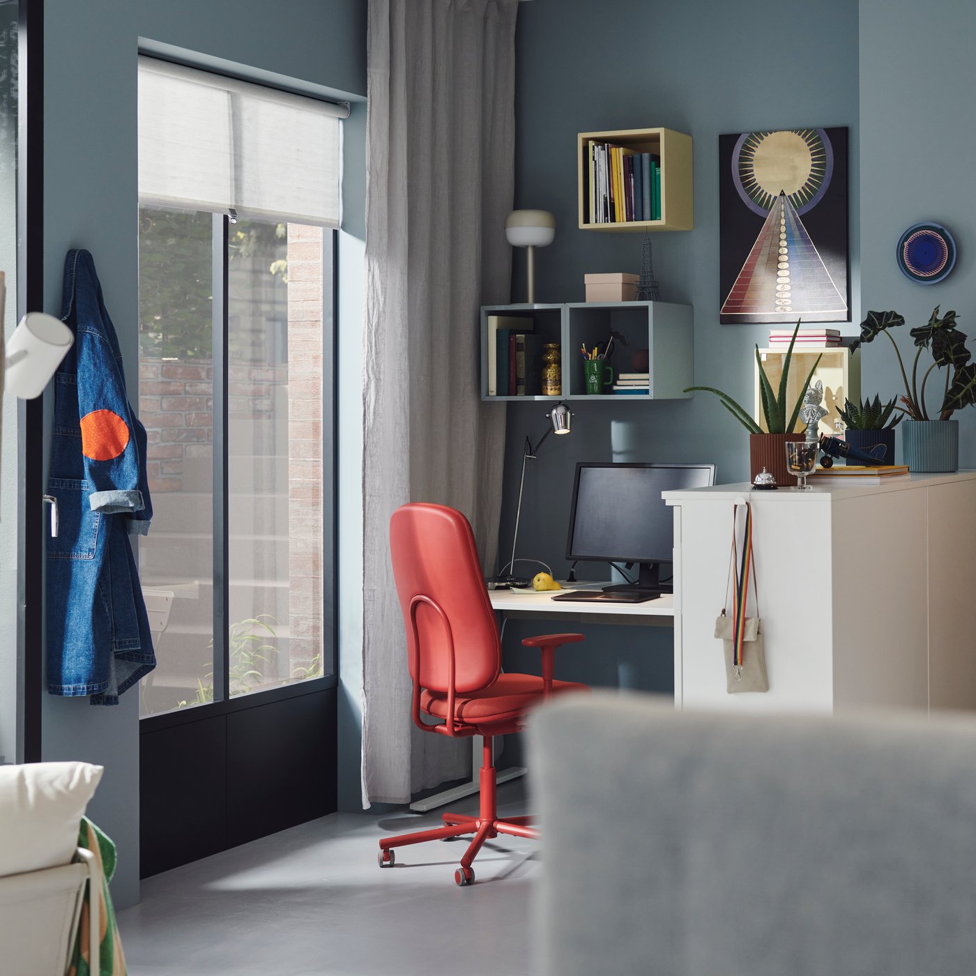 A vibrant office space with blue walls, wall-mounted cabinets in various colours, and SMÖRKULL office chairs in Gräsnäs red.