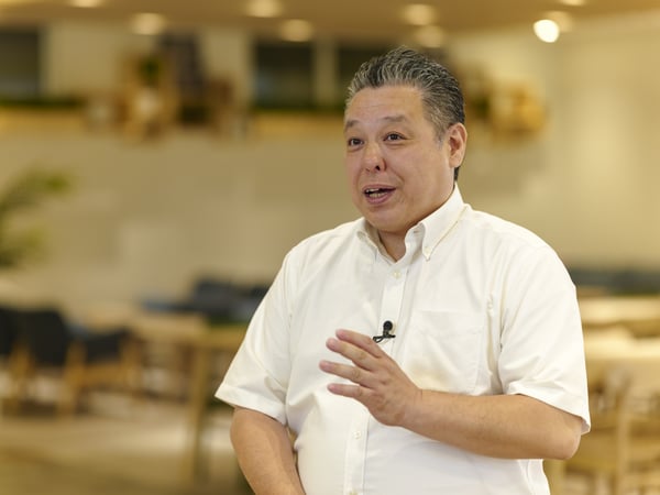 白いシャツを着た人物が、明るい室内でプレゼンテーションを行っている