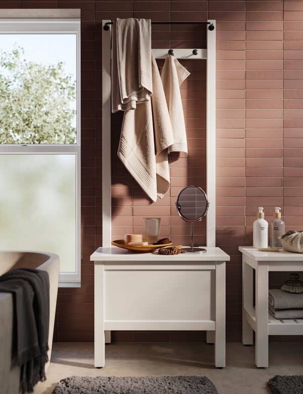 A HEMNES bench in white with diverse bathroom toiletries and a HEMNES storage bench with towel rail with four hooks in white.