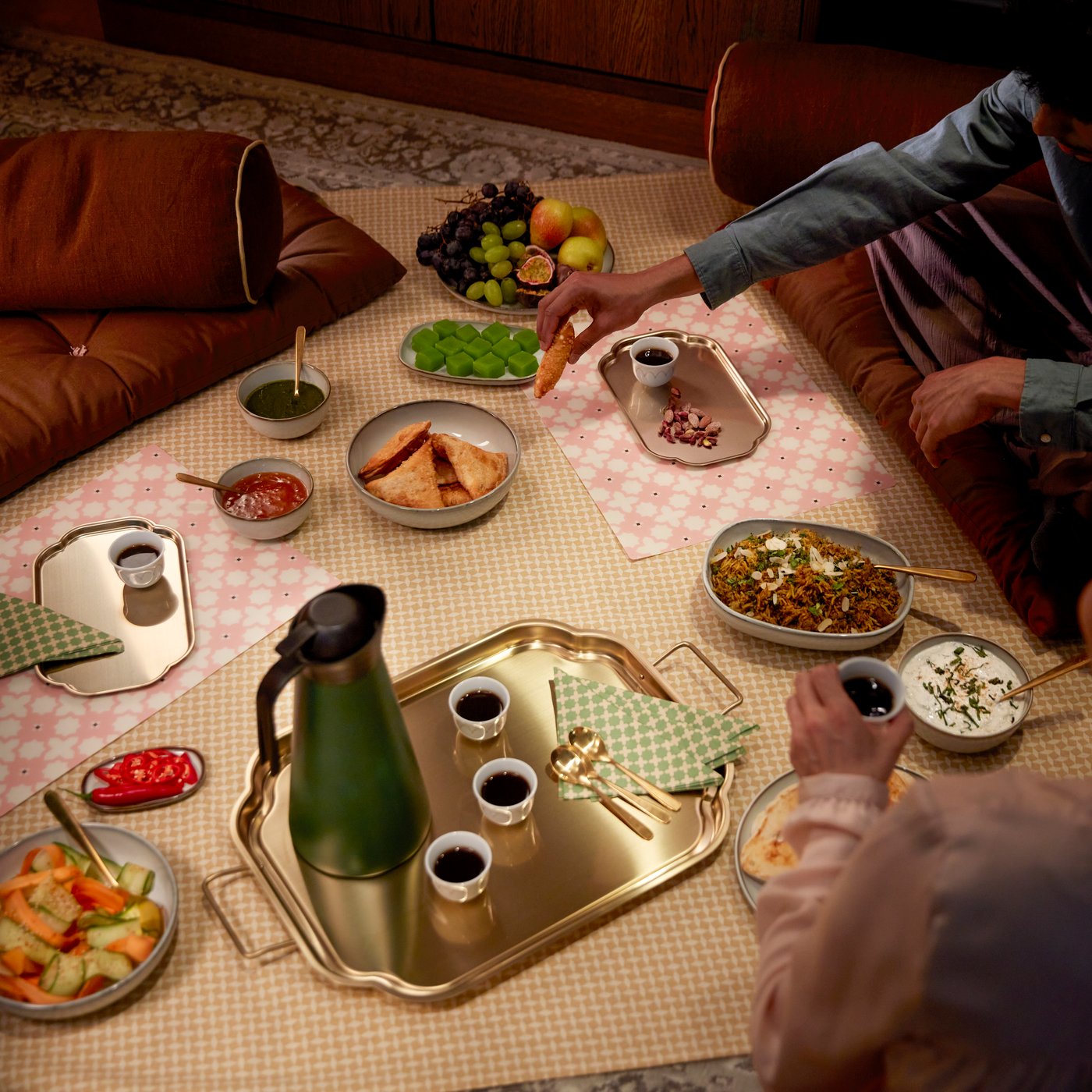 A gold-colour GOKVÄLLÅ serving tray holds diverse items while people enjoy a meal in a cosy, inviting setting.
