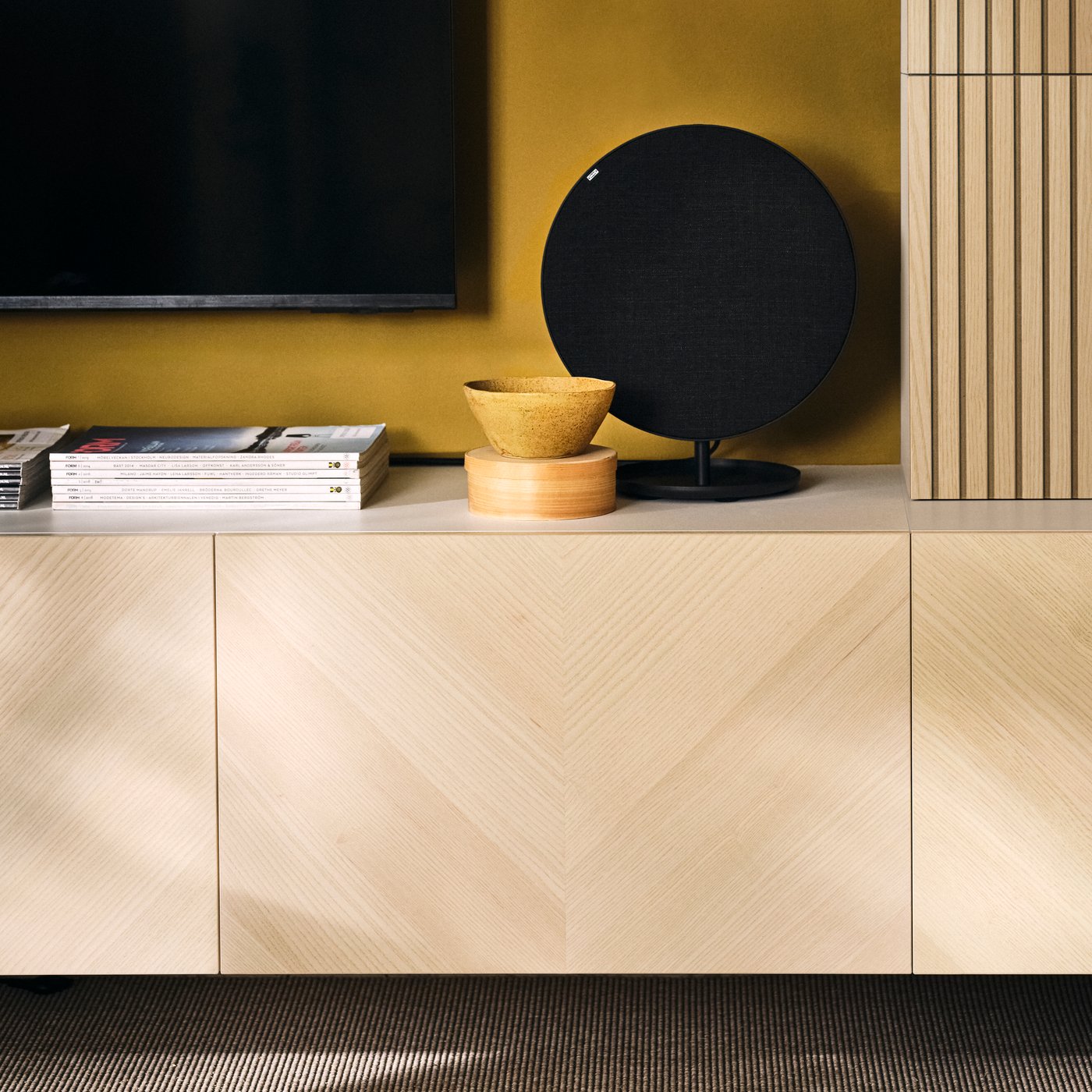 Rangement média BESTÅ avec haut-parleur Bluetooth SOLSKYDD et bols sous un téléviseur dans un salon.