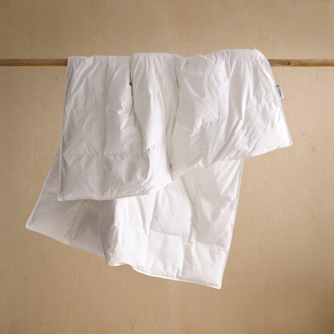 Un edredón blanco sin funda cuelga de una barra sobre un fondo blanco.