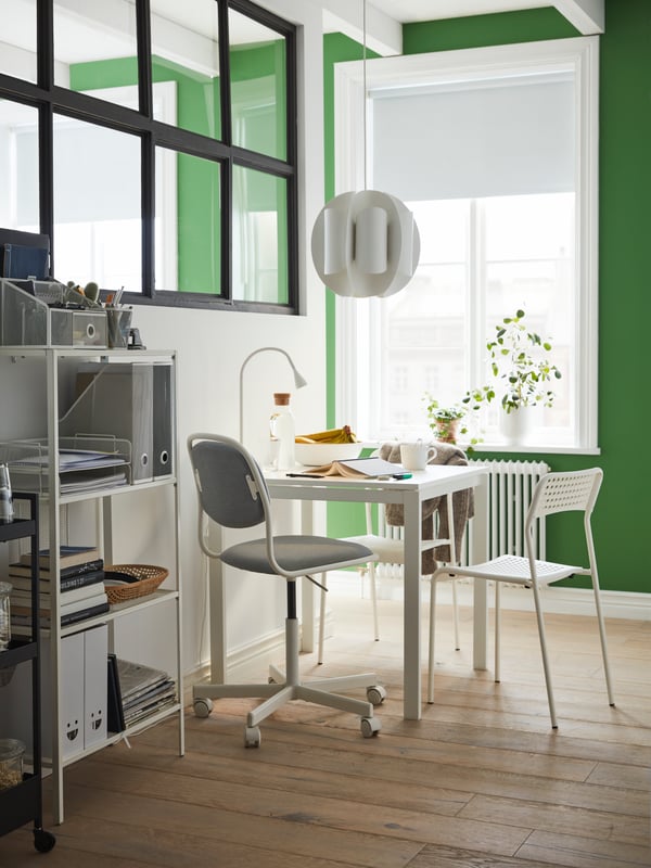 Un comedor pequeño con una mesa cuadrada pequeña con tres sillas distintas. En el costado de la mesa hay un estante de altura media con muchos artículos en su interior.
