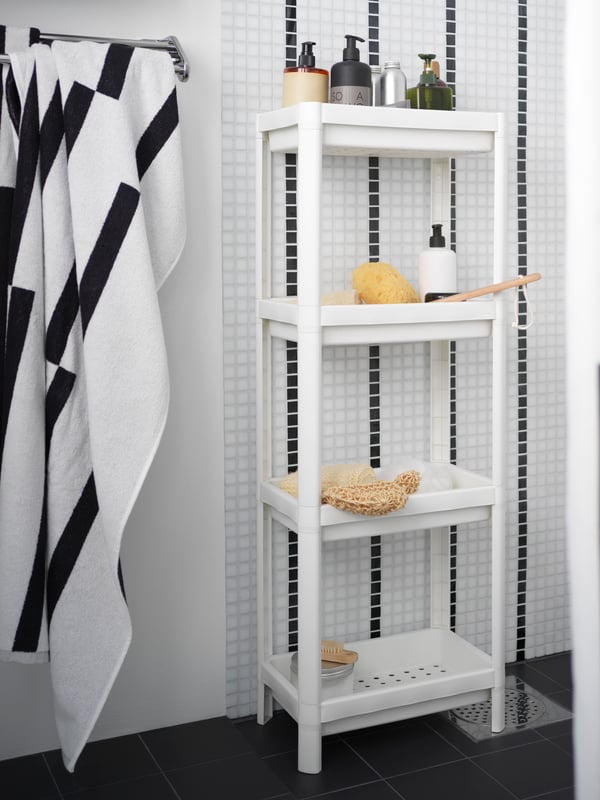 VESKEN bathroom shelf in white with multiple bottles of shampoo and body wash on top, and other shower necessities on different shelves.