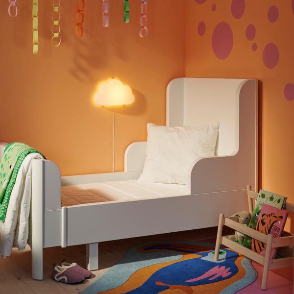 A white BUSUNGE extendable bed in an orange bedroom with a VIMSIG extendable mattress on it and an uncovered cushion pad.
