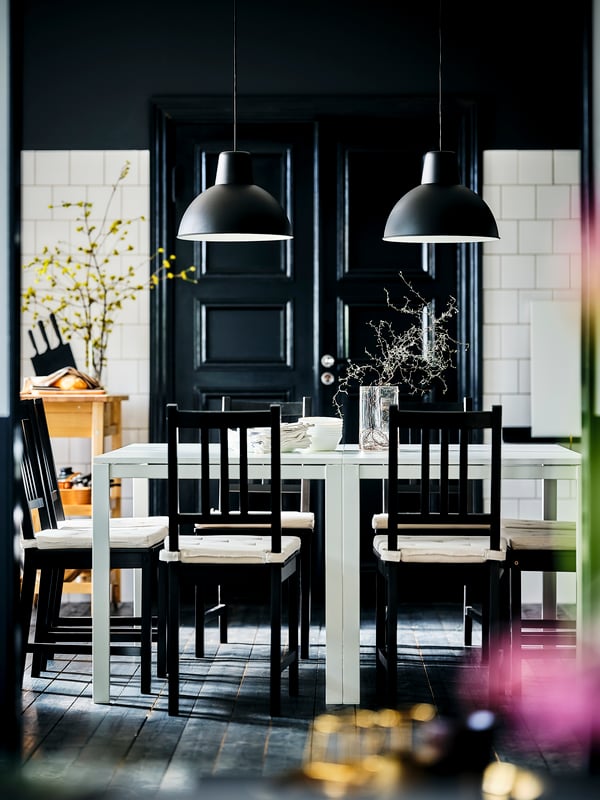 A dining area centred around white MELLTORP tables, brown-black STEFAN chairs, and black SKURUP pendants.