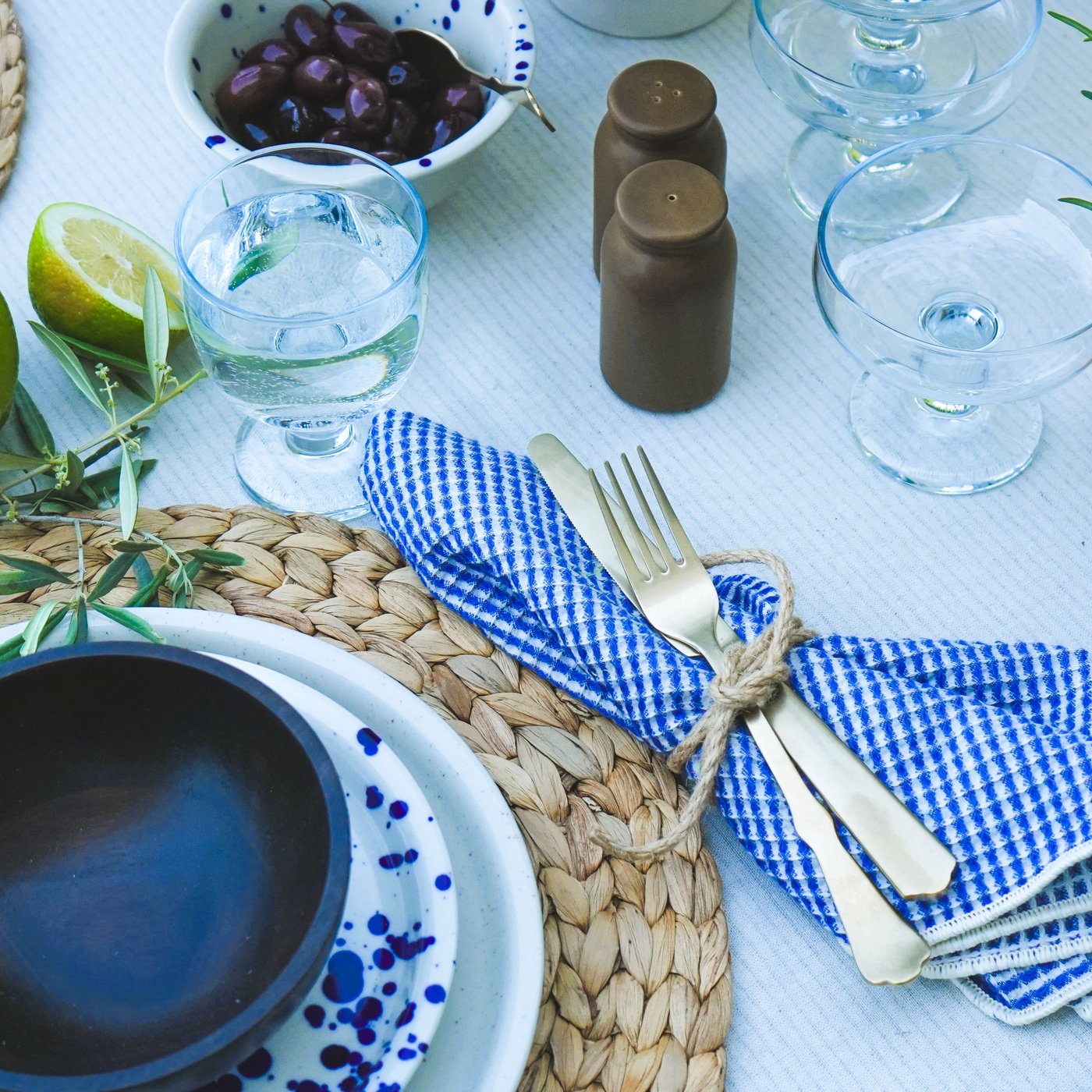 Sommerlich gedeckter Tisch mit NATTKLOT Besteck, Schale mit Oliven, frischen Limetten und Kräutertopf, perfekt für ein mediterranes Essen.