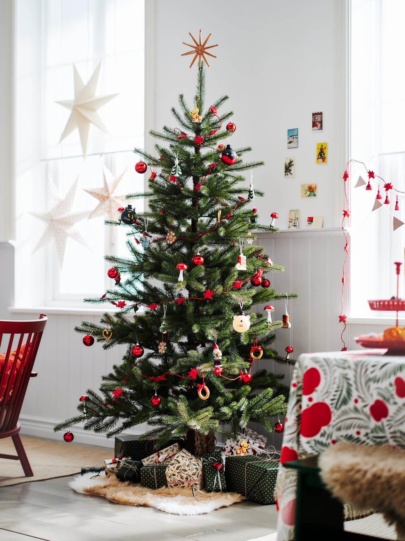 Ruang makan yang terang dengan hadiah berbalut di bawah pokok Krismas buatan VINTERFINT dengan perhiasan VINTERFINT berwarna merah.