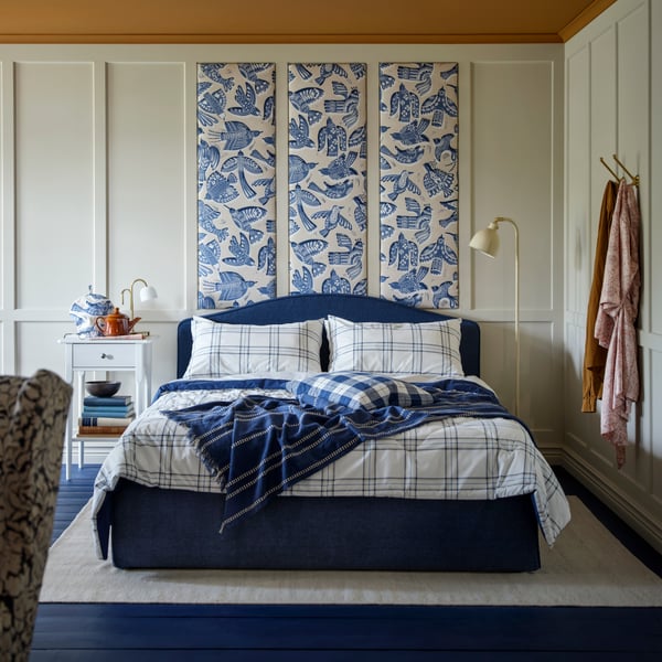 A blue and white LINSNÄRJA comforter set is arranged on a RAMNEFJÄLL upholstered bed frame, with pillows and a throw.