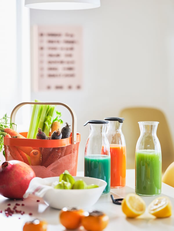 Un plateau blanc avec un panier RISATORP et un mélange de fruits, de légumes et de jus aux couleurs éclatantes dans des carafes en verre transparent.