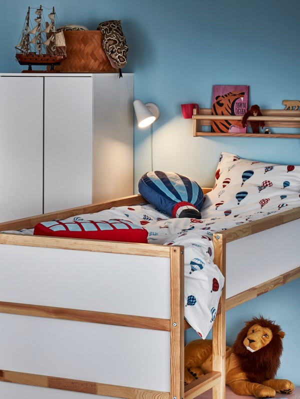 A white and pine KURA reversible bed with UPPTÅG bed linen and colourful UPPTÅG cushions stands in a child’s bedroom.