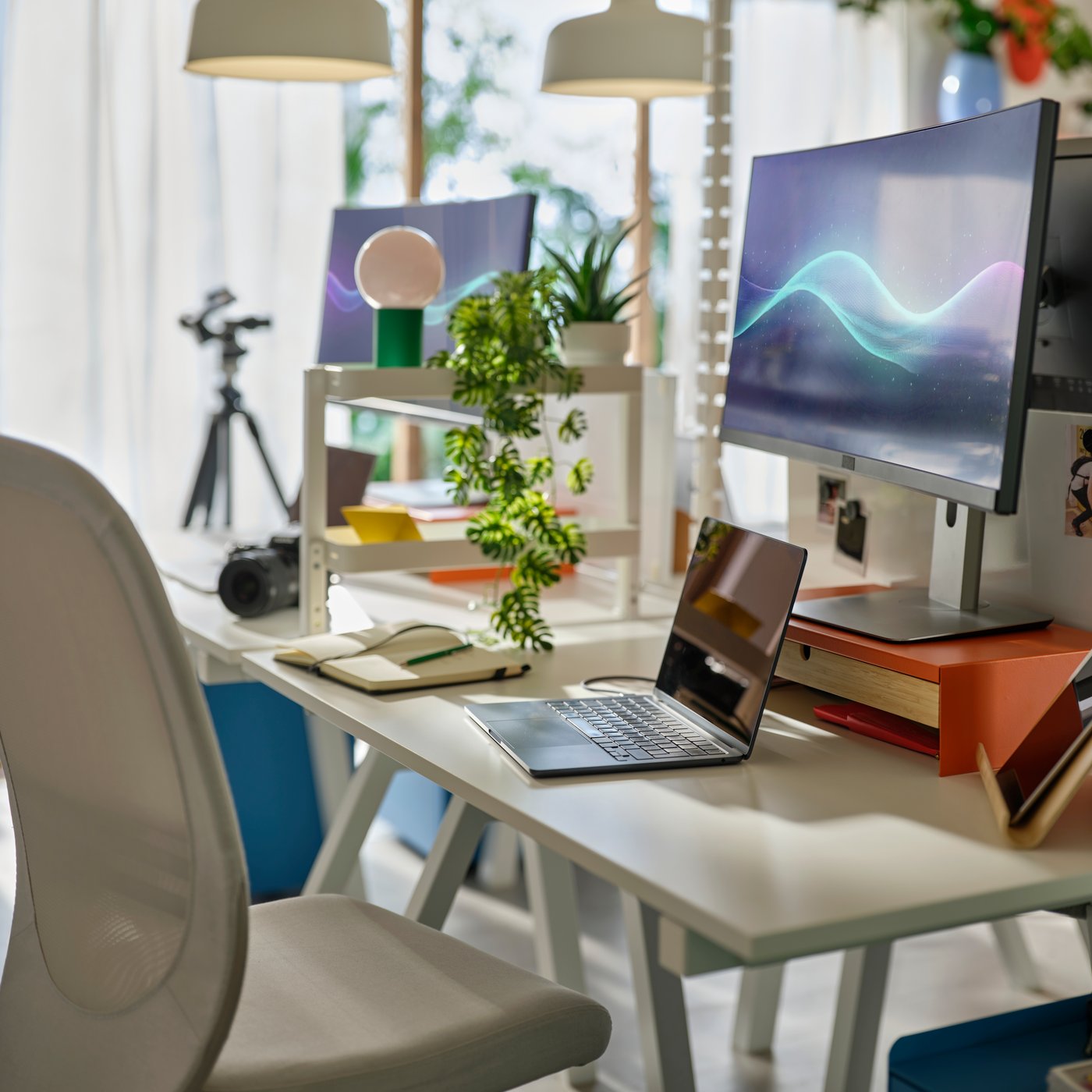 Close up of clutter-free desk with laptop. A large monitor is placed on an orange monitor stand with a storage drawer.
