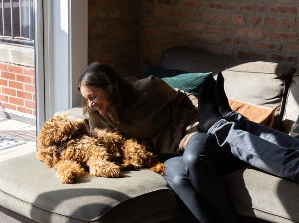 Lady sitting on her sofa, cuddling her small brown dog.